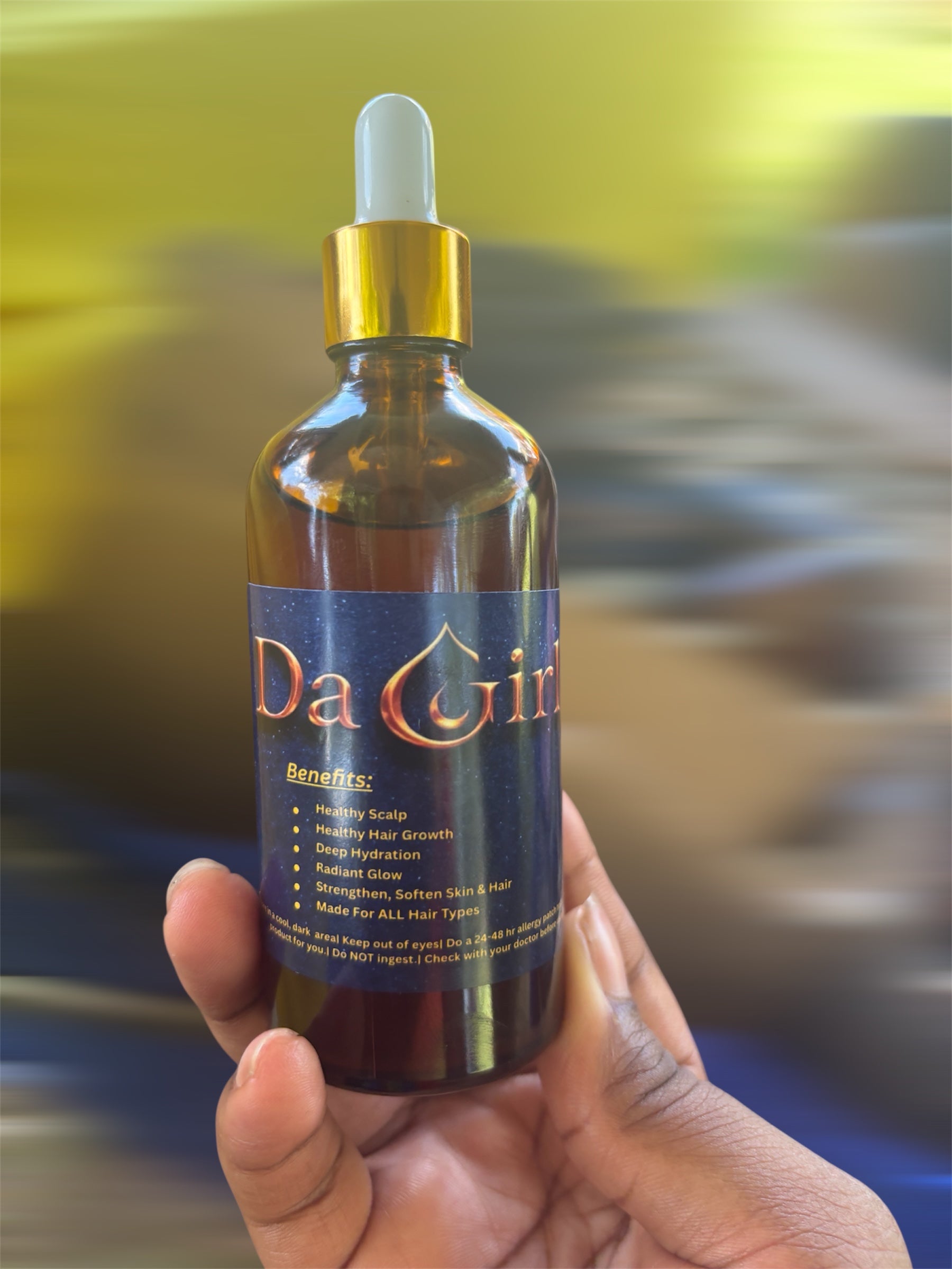 Bottle of 'Da Girls' hair growth oil held in a hand with a blurred background
